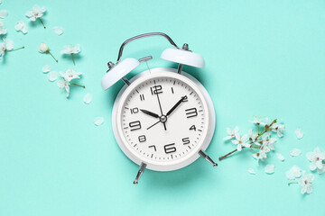 Alarm clock and flowers on turquoise background. Spring time
