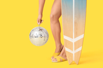 Beautiful woman with surfboard and disco ball on yellow background