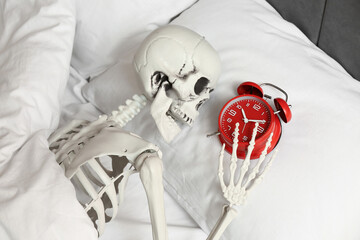 Human skeleton with alarm clock lying in bed, closeup