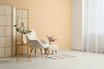 Interior of stylish living room with white armchair, pouf and blooming tree branches on coffee table