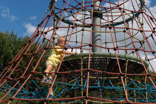Little boy climbing rope pyramid at outdoor playground on sunny summer day. Concept of childhood adventure, active lifestyle and kids recreational activities. High quality photo