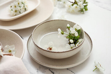 Clean beige plates with blooming flowers on white background, closeup