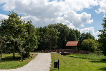 Scenic park landscape with a wooden bridge, green grass, trees, and a clear blue sky on a sunny...