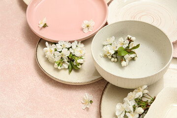 Different clean plates with blooming flowers on light pink background, closeup