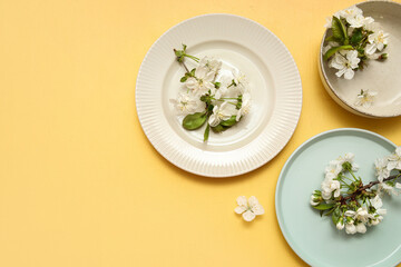 Different clean plates with blooming branches on yellow background