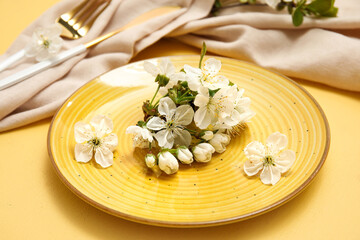 Beautiful table setting with blooming branch on yellow background, closeup