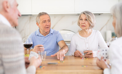 Group of four mature friends is playing card game poker. Two married couples pensioners have fun...