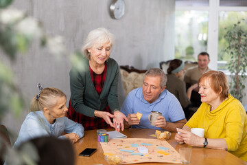 Happy elderly woman playing board game with group of friends at table. Concept of socialization of...