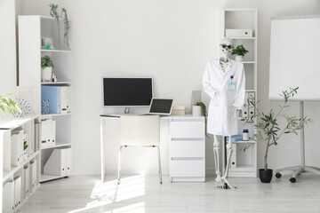 Interior of light hospital with human skeleton model in doctor uniform and modern computer on table