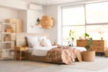 Blurred view of stylish bedroom with comfortable bed, wooden furniture and houseplants