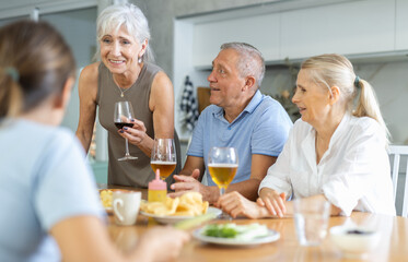 Group of joyful seniors at family dinner drinking and chatting at table in kitchen