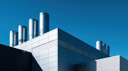 Fototapeta premium Contemporary industrial facility with metal ventilation pipes on rooftop against clear blue sky. HVAC system. Clean energy infrastructure and modern manufacturing architecture