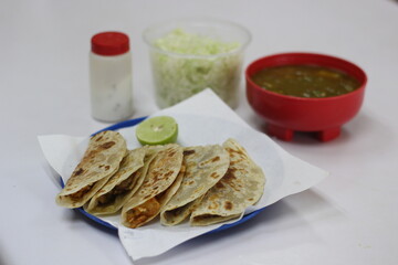 An inviting plate of handmade tacos filled with a variety of mexican creations, fresh lettuce, lime, and accompanied by green sauce for a delightful eating experience.