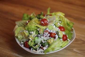 A vibrant salad featuring cherry tomatoes, fresh greens, and creamy avocado topped with crumbled...