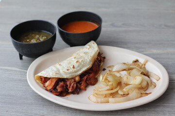 A rich and savory al pastor taco filled with grilled meat and accompanied by sides of sauces and grilled onions, offering an authentic taste of traditional Mexican street food.