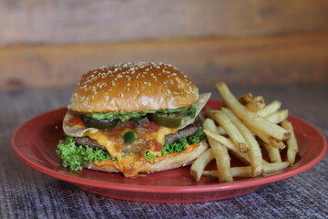 A delicious hamburger stacked high with fresh toppings, including cheese, jalapeños, and lettuce, served alongside a crispy portion of golden fries on a red plate.