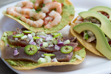 A colorful arrangement of three tostadas topped with succulent shrimp, creamy avocado slices, and zesty garnishes, perfect for seafood lovers and taco enthusiasts alike.