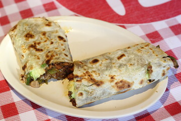 A freshly prepared burrito featuring grilled vegetables and a variety of flavors, served on a classic plate with a checkered pattern for an inviting presentation.