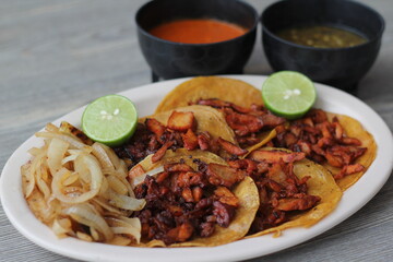 An inviting platter of tacos al pastor topped with savory meat, accompanied by grilled onions, lime...