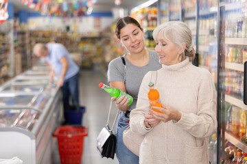 Mom with adult daughter choose and buy bottles of carbonated drink in the supermarket.
