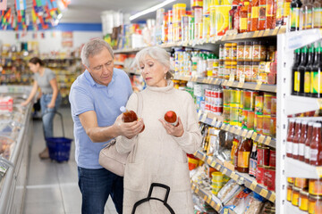 Elderly couple choosing hot chili sauce together in the grocery section of a supermarket