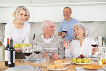 At the table, happy group of adults enjoy their holiday, drink red wine and talk together