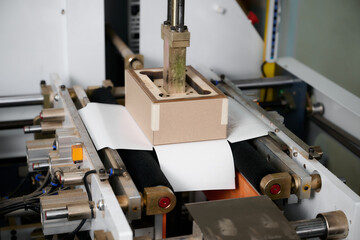 Semi-automatic wrapping machine efficiently encases rectangular boxes in a bustling production facility