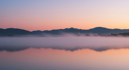 Fototapeta premium Dreamy dawn over a tranquil lake with mist and mountainous reflections