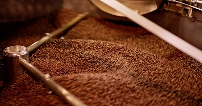 Rightward panning shot showing espresso beans rotating inside a cooler, gradually revealing the roasting drum. Scene captures the movement, texture, and heat dispersion of the final roasting stage.