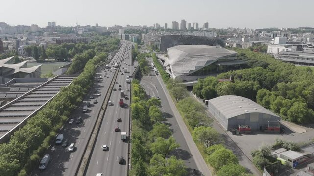 Drone footage advancing over the Paris ring road (p&eacute;riph&eacute;rique), showcasing buildings, greenery, and distant skyscrapers in the Paris suburbs - France