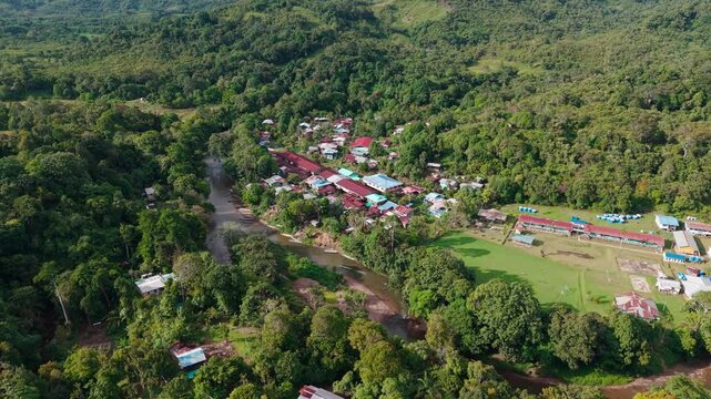 Wide drone perspective of the Upper Baram river curving around Long Lamai settlement with surrounding emerald hills under soft daylight.