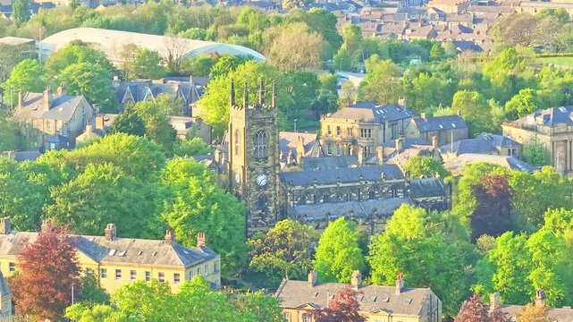 Huddersfield city centre revealing St Peter's Parish Church with its clock tower surrounded by Georgian buildings, tree-lined streets, and nearby Springwood area under soft light, drone static shot