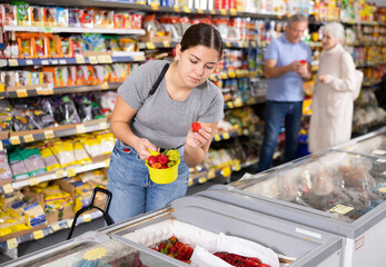 Young woman shopping for frozen strawberries in the grocery section of a supermarket