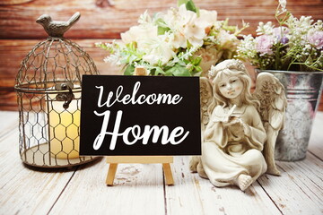 Welcome Home text on easel with alarm clock and flowers decoration on wooden background