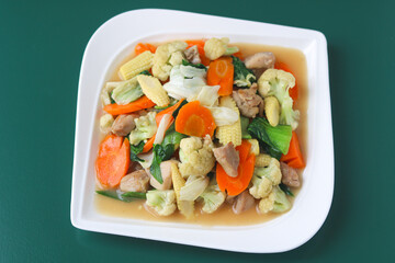 Top view of Capcay. A halal Indonesian-Chinese stir-fry food packed with colorful vegetables and tender chicken. Served fresh on a white plate with a green background.