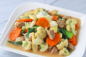 A vibrant close-up of Capcay. A halal Indonesian-Chinese stir-fry food packed with colorful vegetables and tender chicken. Served fresh on a white plate with a marble background.
