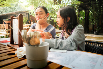 Asian mother and teen daughter looking at restaurant menu, discussing on and choosing meals for lunch