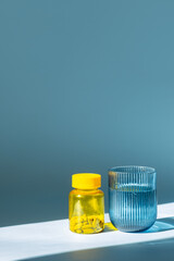 Yellow Vitamin Bottle and Ribbed Glass of Water Illuminated by Strong Sunlight. Taking Supplements for Wellbeing.