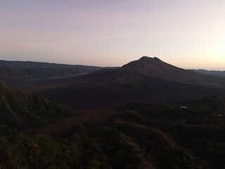 Stunning drone shot of Lake Batur at dawn, with mountain silhouettes reflecting on calm water under a colorful sky
