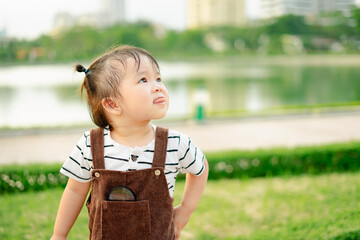 Young child gazing at the sky in a park on a sunny day, surrounded by greenery and city buildings...