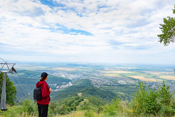 Woman hiker standing on mountain trail, looking at forested hills.