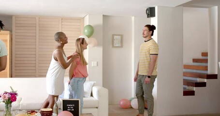 Friends celebrating new job with cake and balloons in living room, smiling happily
