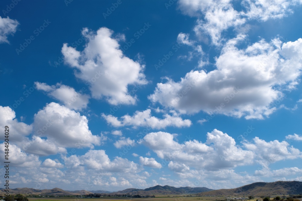Aufkleber bright blue sky filled with fluffy white cumulus clouds above a sunny landscape of rolling hills and