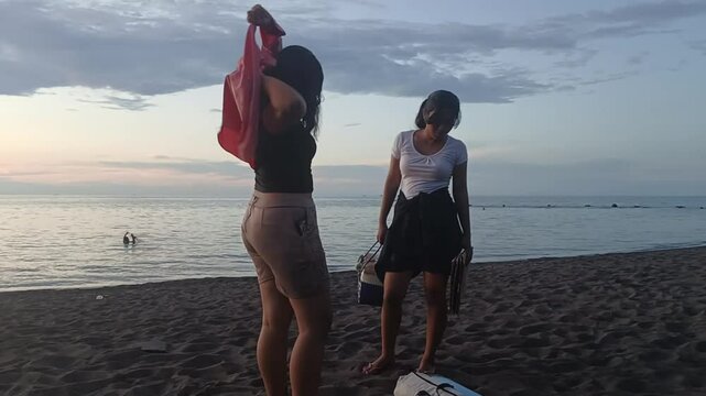 Two teen girls talk and get dressed while packing up their tent and belongings at the beach.