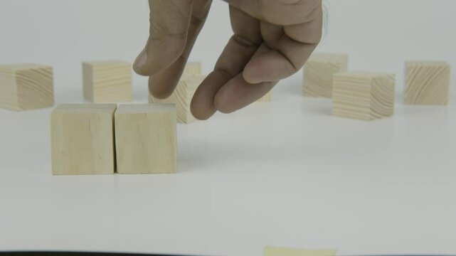 A hand places a wooden block with the number six next to another block on a white background, conveying a sense of numeric sequence, steady progress, or organization in a minimal and clean setting