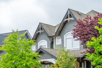Top of grey stucco luxury house with shingle roof, green trees and nice windows in Spring in Vancouver, Canada, North America. Day time on April 2025.