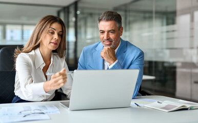 Two executive leaders team using laptop working on computer at work desk, busy happy middle aged...