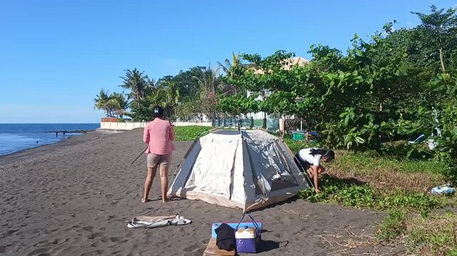 The girls work together to firmly place pegs and prepare the tent structure under intense sunlight.