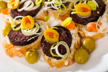 Image of tasty canapes with blood sausage, bread, olives and onion at plate