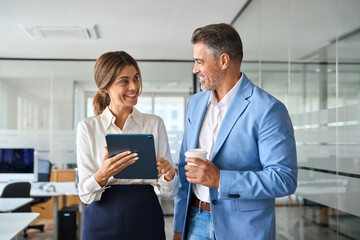 Two happy middle aged business man and woman executives partners, 2 professional mature business people team working together checking corporate results collaborating standing in company office.